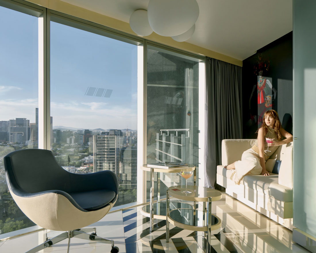 A woman sitting on a couch in a room with large windows.