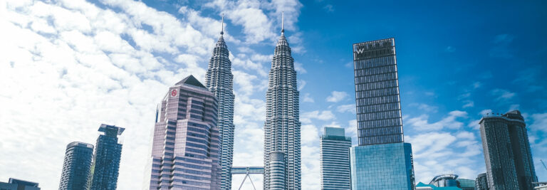 El perfil urbano de Kuala Lumpur, con las Torres Gemelas Petronas y los modernos rascacielos que las rodean, bajo un cielo luminoso y parcialmente nublado.