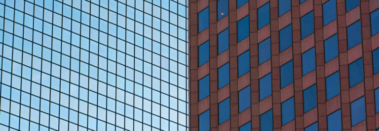 Two contrasting buildings side by side; one with a blue glass facade and the other with a red brick exterior, showcasing a blend of modern and traditional architecture.