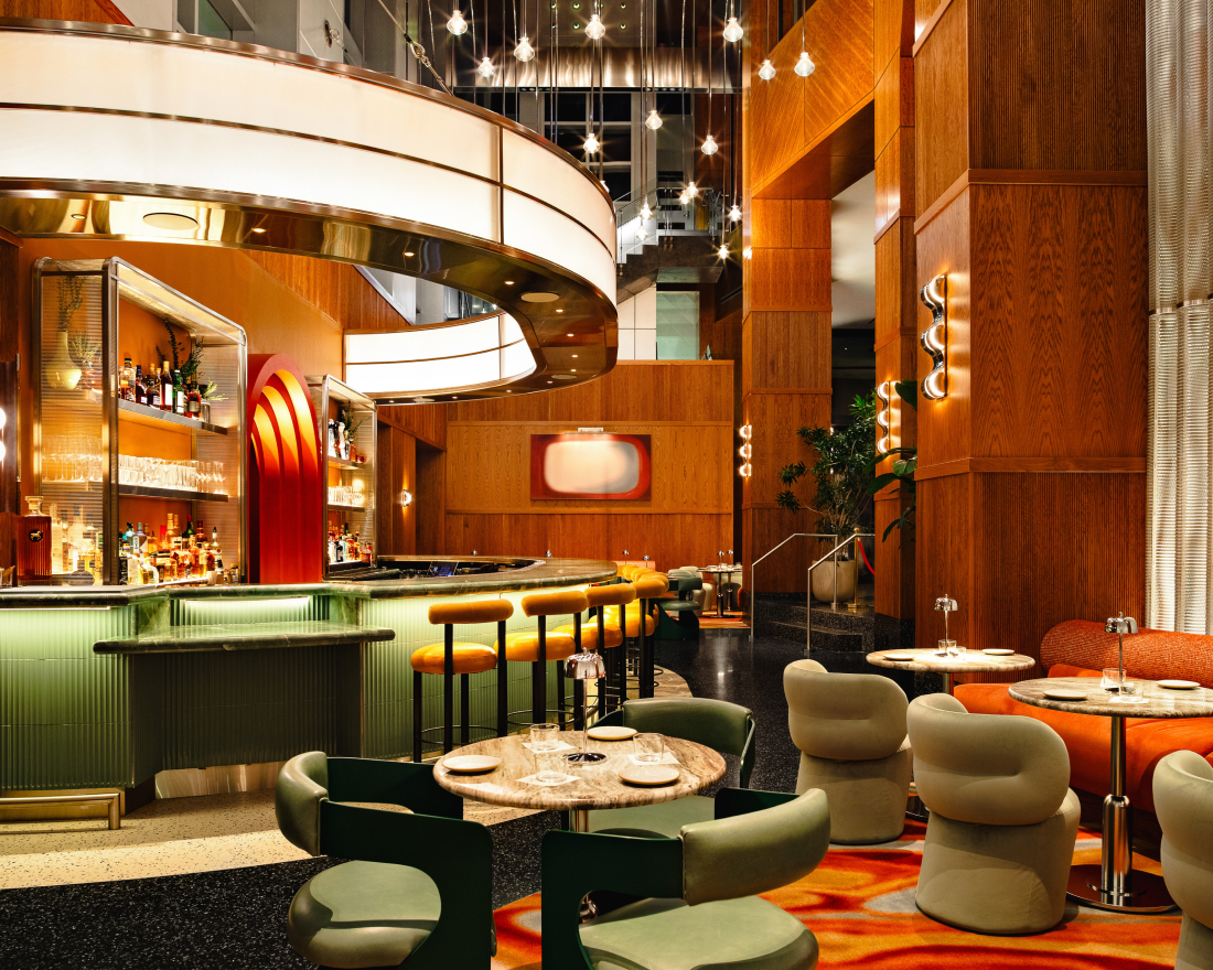 A high-end bar and dining area with a curved green bar, circular tables, modern green and tan chairs, and warm wood-paneled walls.