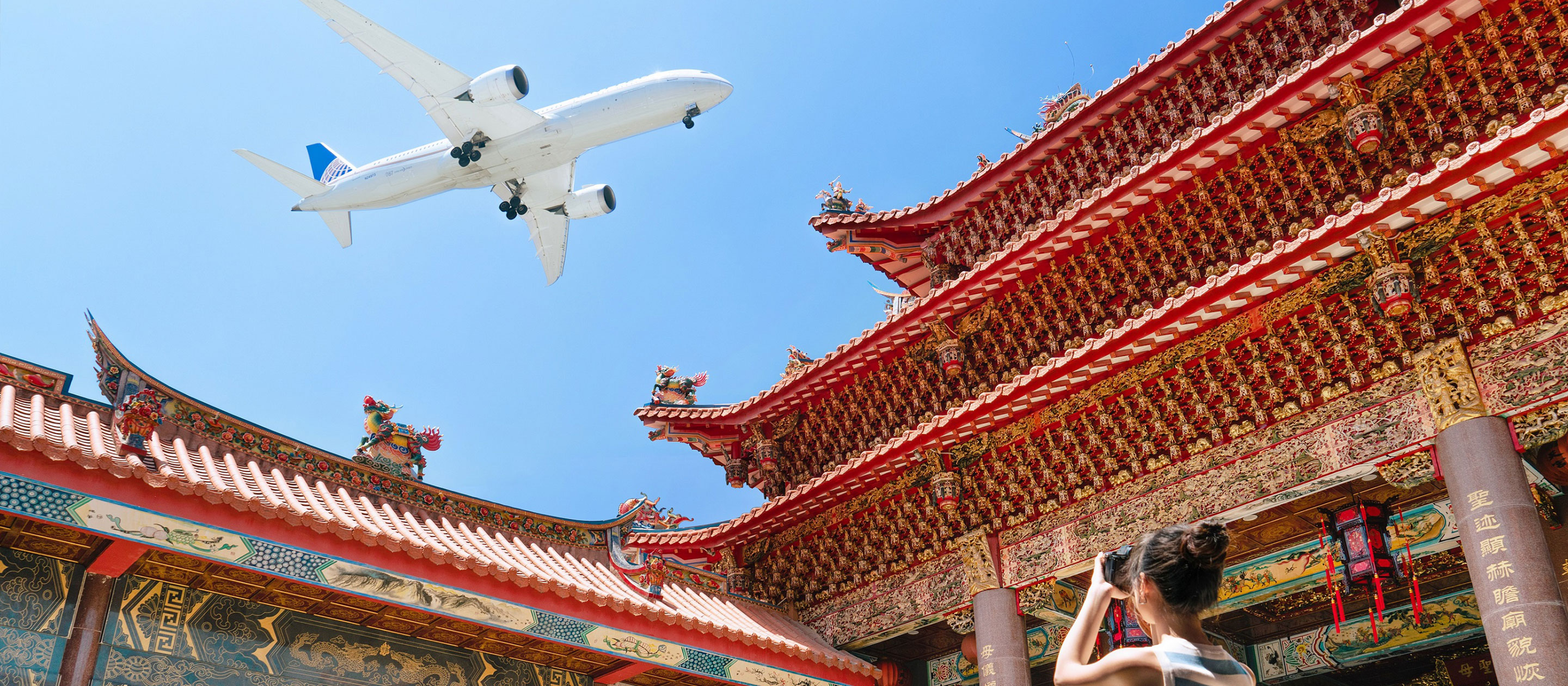 Una persona toma una fotografía de un gran templo decorado con gran delicadeza y detalles en rojo y dorado. Encima, un avión blanco vuela por un cielo azul claro. La escena combina la arquitectura tradicional con los viajes aéreos modernos.