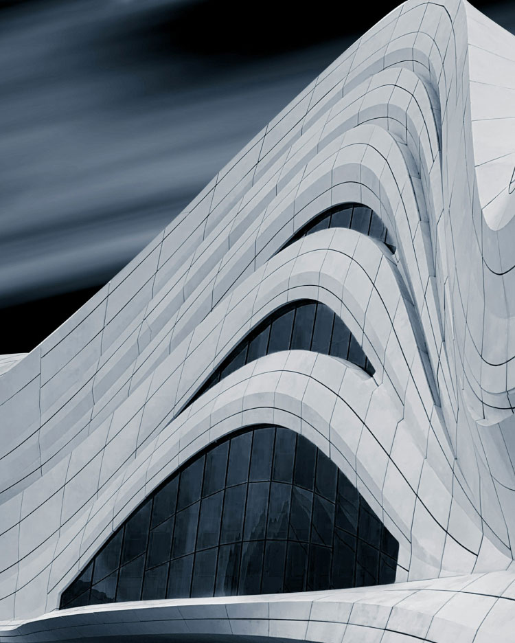 Estructura arquitectónica curva y moderna con líneas fluidas y grandes ventanas arqueadas, frente a un cielo oscuro y borroso.