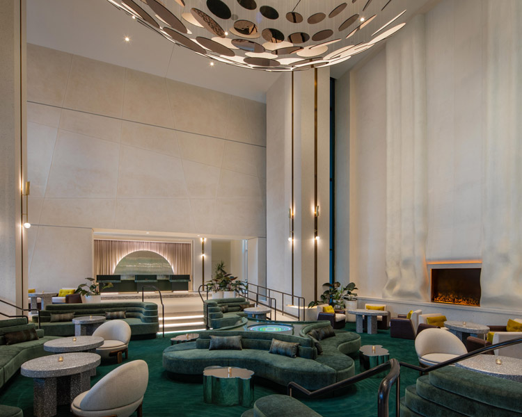 Eine moderne Hotellobby mit Sitzgelegenheiten aus grünem Samt, runden Tischen, einem eleganten Kamin, hohen weißen Wänden und einer dekorativen Deckengestaltung. Die warme Beleuchtung und das minimalistische Dekor schaffen eine einladende, luxuriöse Atmosphäre.