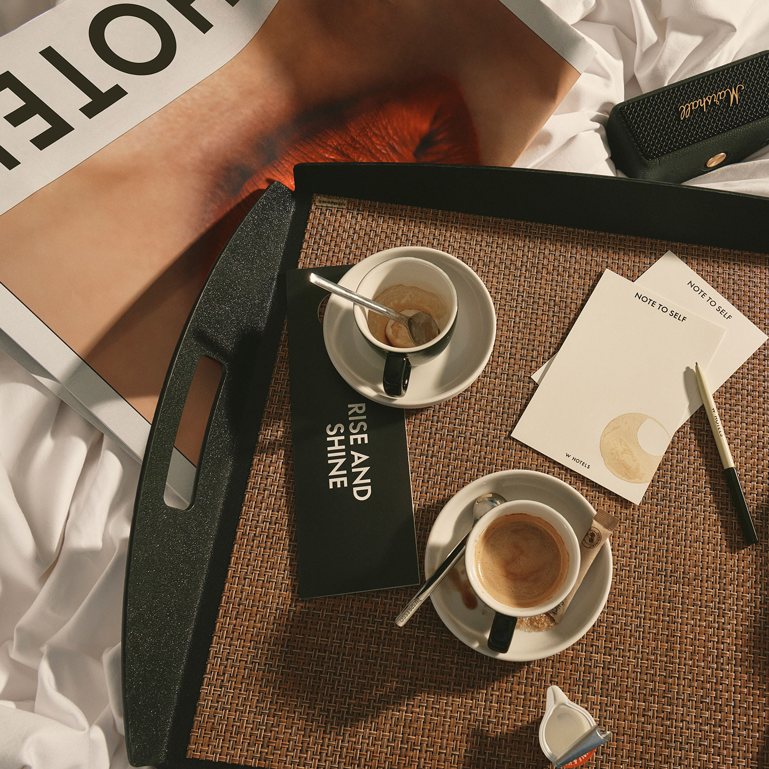 Auf einem Frühstückstablett auf dem Bett stehen zwei Espressotassen, ein Löffel, eine Notizkarte, ein Stift, ein Büchlein mit dem Titel 