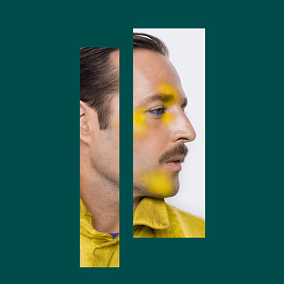 A man with slicked-back hair and a mustache, wearing a yellow shirt and yellow face paint, is shown in a split portrait with two vertical sections on a teal background.