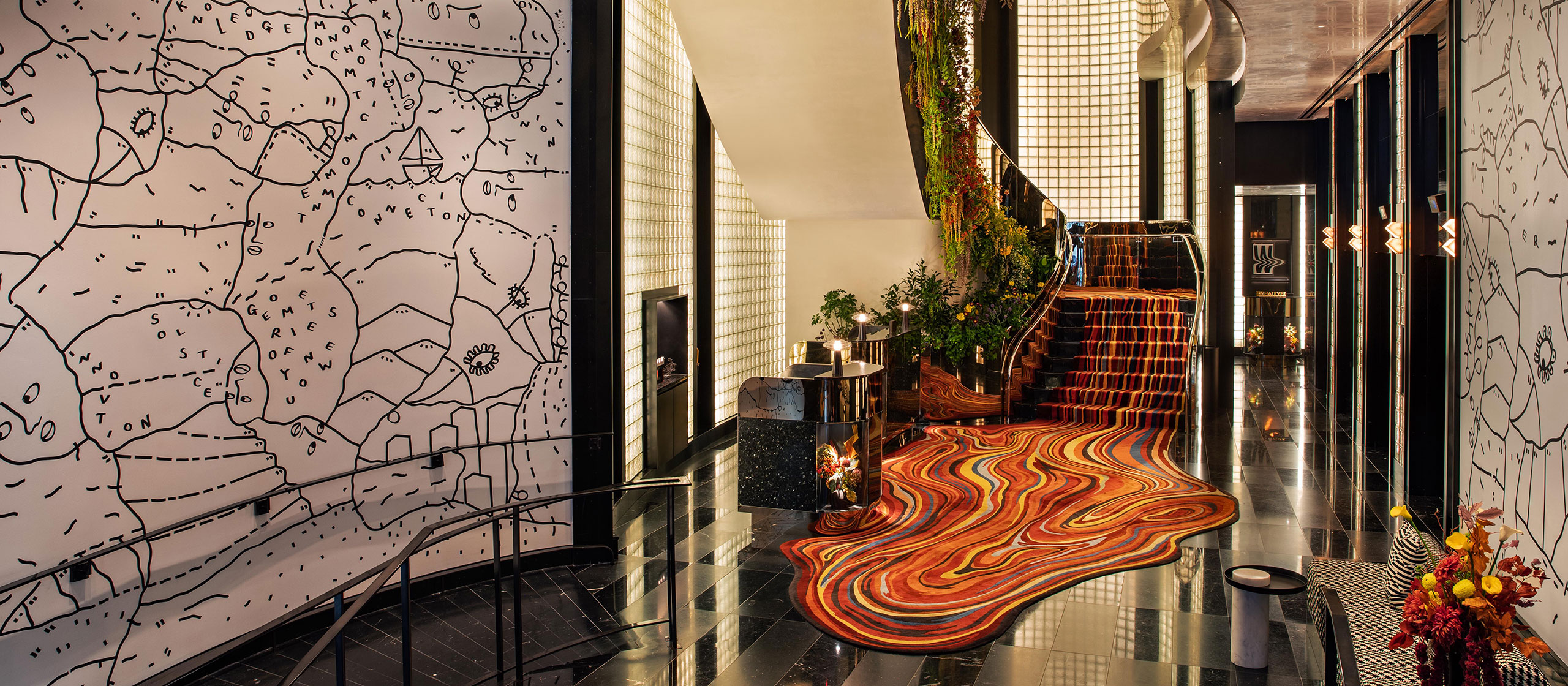 Eine moderne Hotellobby mit glänzenden schwarzen Böden, einem gewellten rot-orangenen Teppich, einer Wand mit einer Landkarte und einer mit Grün und Pflanzen geschmückten Treppe. Der Raum ist hell erleuchtet und hat ein stilvolles, modernes Design.