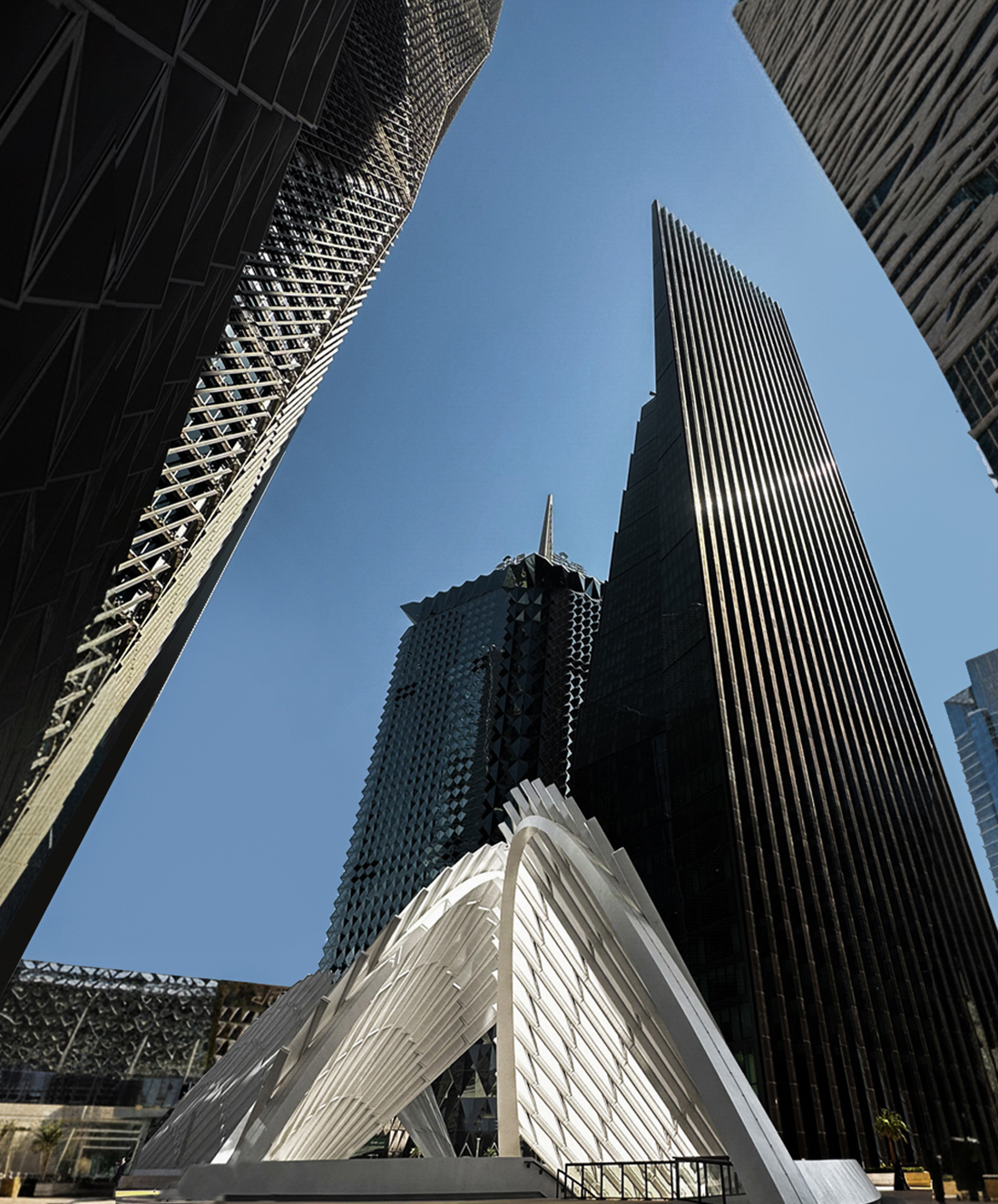Several modern skyscrapers with unique geometric designs rise against a clear blue sky, surrounding a white architectural structure with curved, ribbed arches in the foreground.